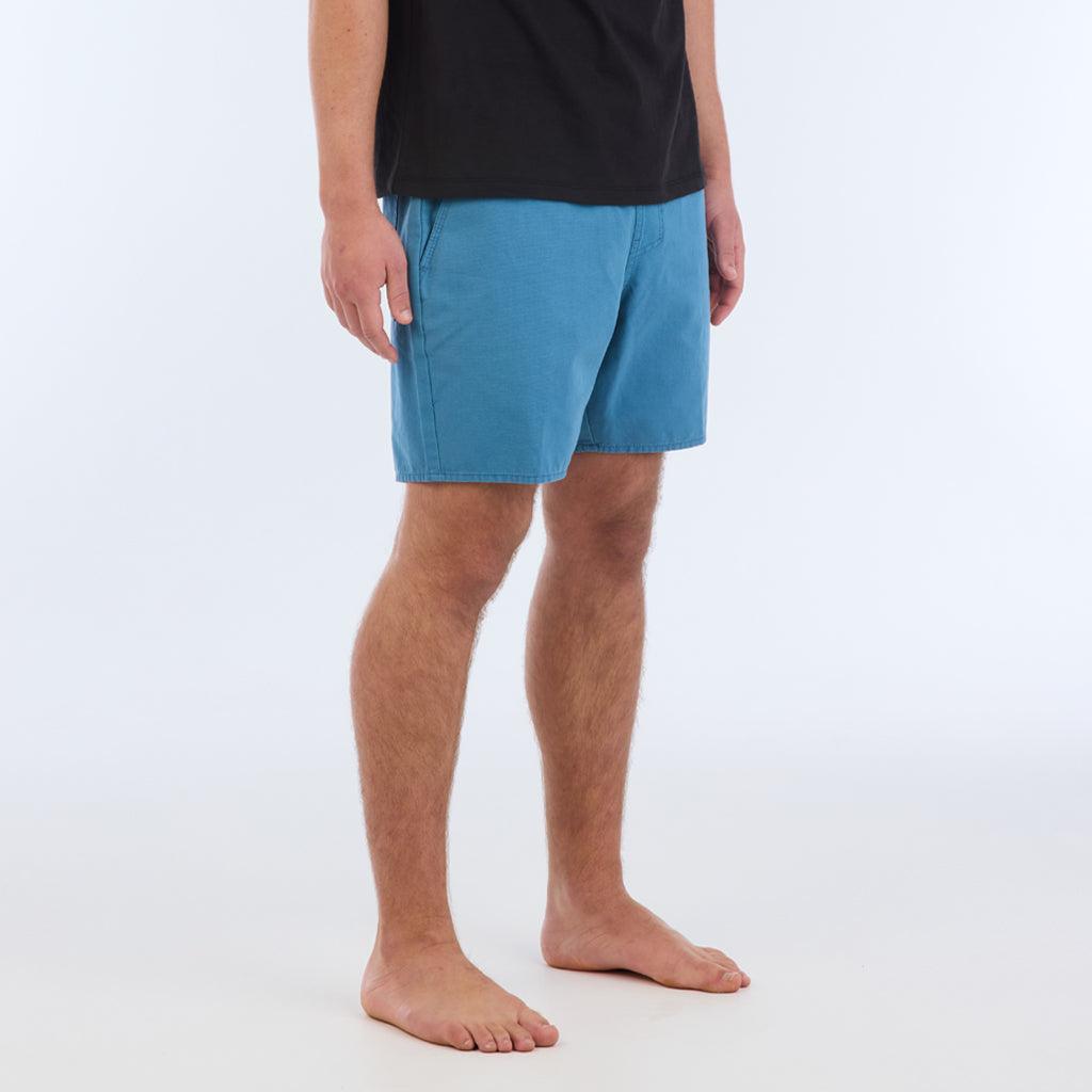 on model with black top, side view:The Foundation Walkshort is a classic walkshort silhouette that comes in at a 17” length. It features a solid blue coloring, and features an elastic waistband and drawcord. The pocketing is two side pockets and two back patch pockets. It features the signature smaller IPD flag label on the lower left leg.