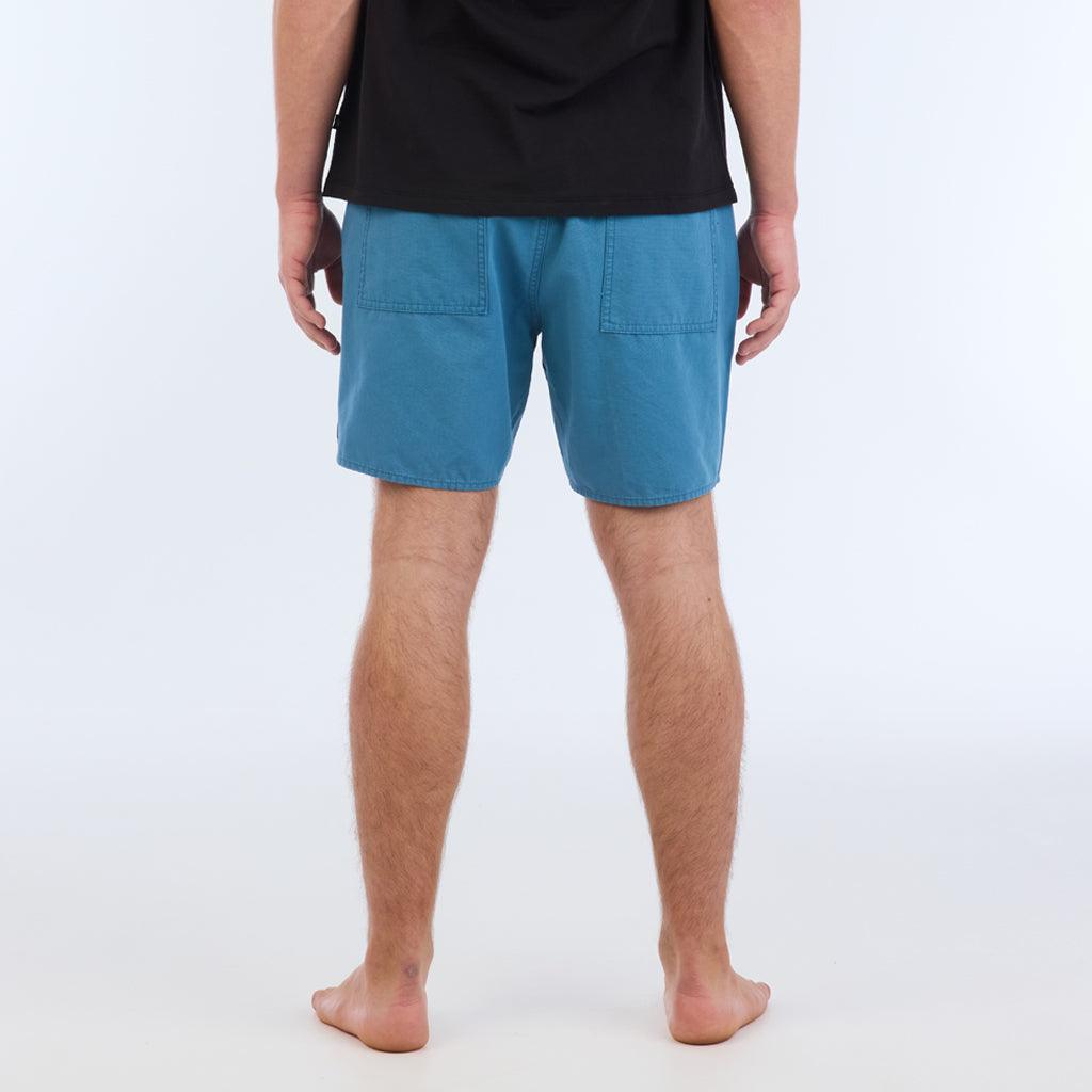 on model with black top, back view:The Foundation Walkshort is a classic walkshort silhouette that comes in at a 17” length. It features a solid blue coloring, and features an elastic waistband and drawcord. The pocketing is two side pockets and two back patch pockets. It features the signature smaller IPD flag label on the lower left leg.