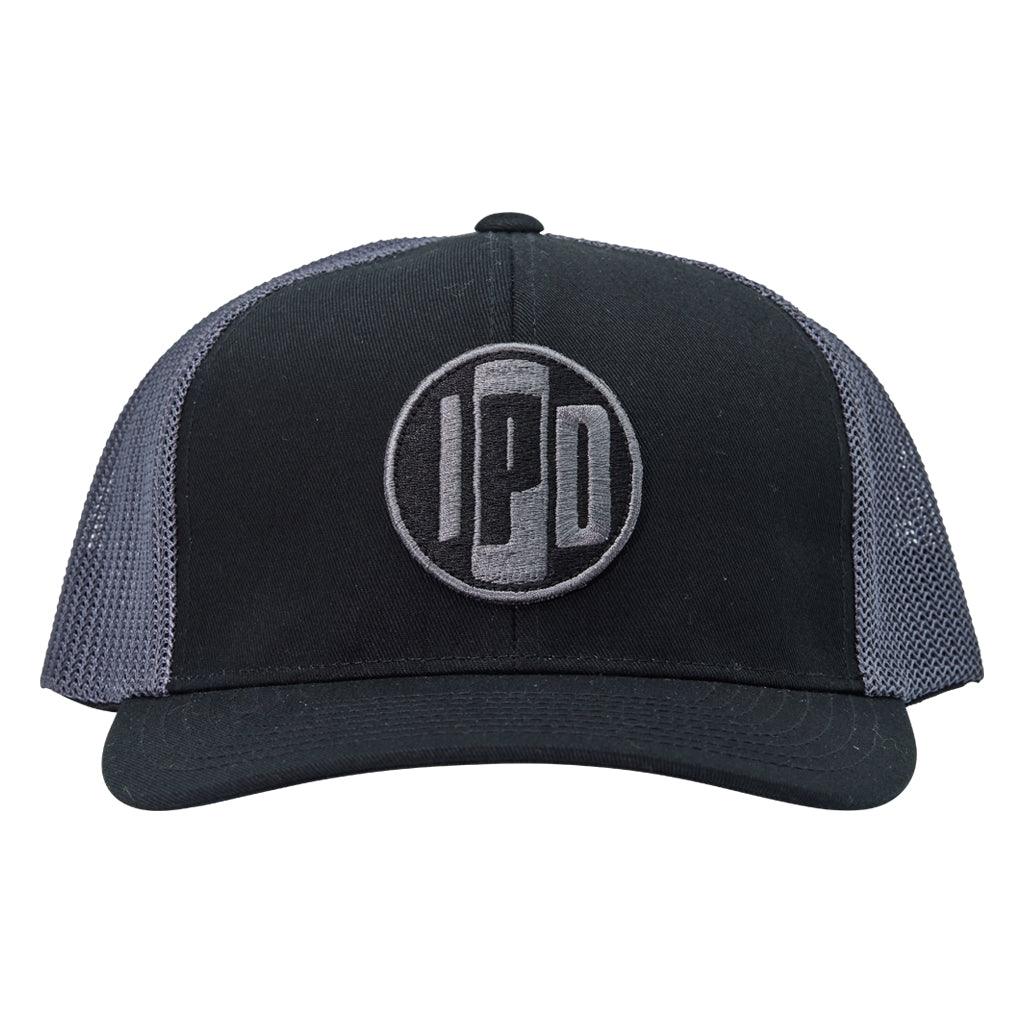 A structured trucker hat with white mesh on the back and a cotton twill white front. In the middle of the front is an embroidered IPD black and white patch logo. This hat has a curved brim and adjustable snap back. 