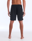 The HI 83 Solid Scallop boardshort on male model features an 18” length and an all black coloring, delivering maximum comfort in a minimalist look. It also has a waistband tie, back patch pocket, and a black IPD logo patch halfway up the left leg taping