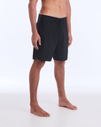 The HI 83 Solid Scallop boardshort on male model features an 18” length and an all black coloring, delivering maximum comfort in a minimalist look. It also has a waistband tie, back patch pocket, and a black IPD logo patch halfway up the left leg taping