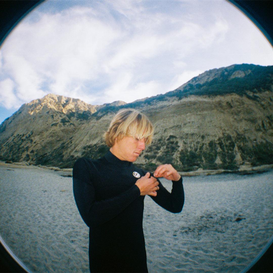 Blonde  man surfer attaches zipper on left shoulder of 3M front chest zip full body wetsuit